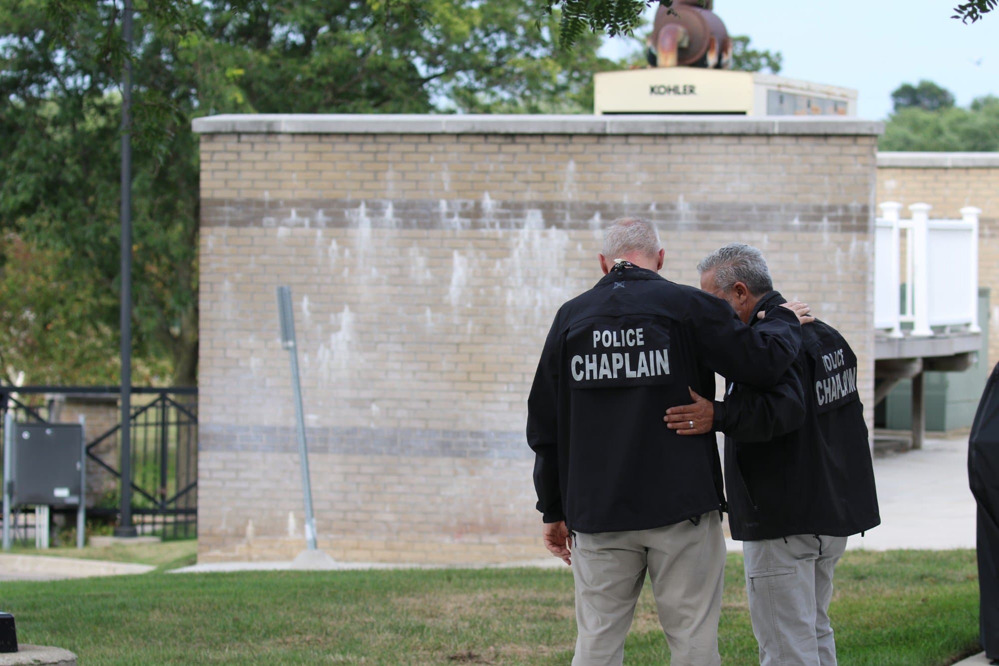 Two police chaplains walking together outside a station, one supporting the other
